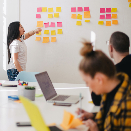 Photo of a woman in a classroom placing sticky notes on a board