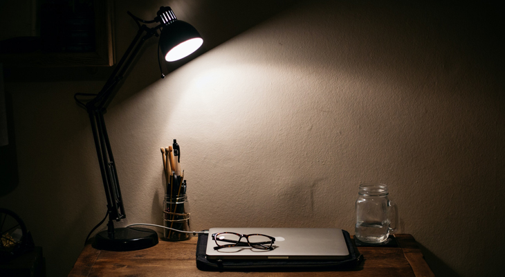 Photo of a closed laptop on a table with a small lamp shining light